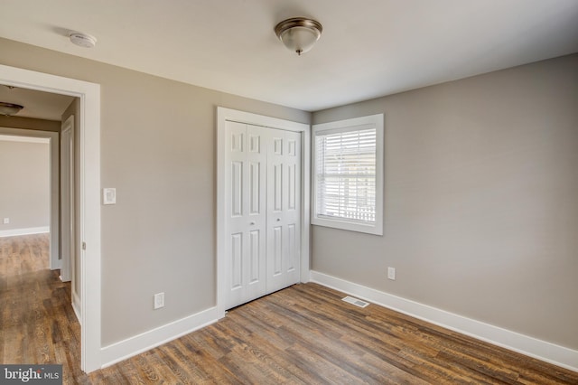 unfurnished bedroom featuring dark wood-style floors, visible vents, a closet, and baseboards