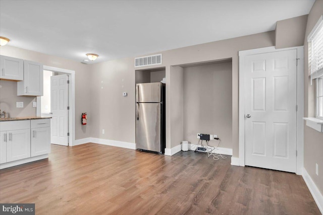 kitchen with visible vents, a sink, freestanding refrigerator, light wood finished floors, and baseboards