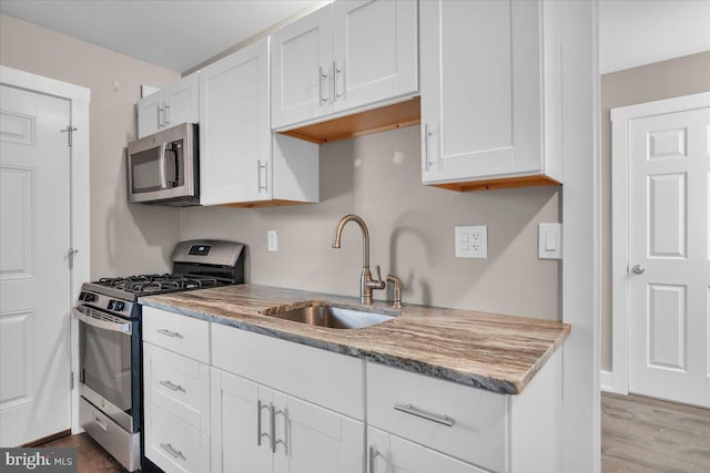 kitchen with a sink, light stone countertops, white cabinetry, and stainless steel appliances