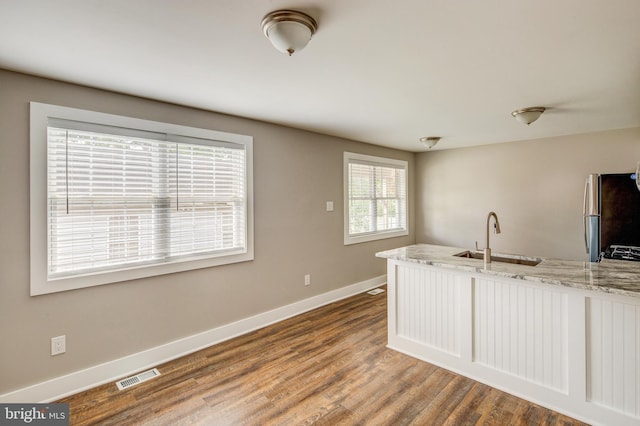 kitchen featuring light stone counters, wood finished floors, visible vents, freestanding refrigerator, and a sink