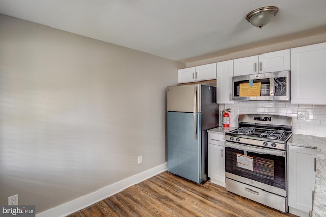 kitchen with light stone counters, backsplash, wood finished floors, white cabinetry, and appliances with stainless steel finishes