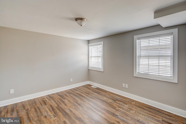 empty room featuring dark wood-type flooring, visible vents, and baseboards