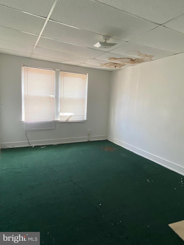 carpeted empty room featuring a paneled ceiling and baseboards