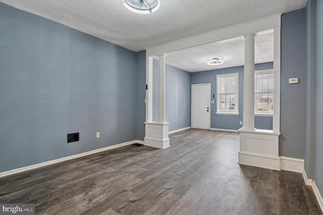 foyer entrance with baseboards, a textured ceiling, dark wood-style floors, and ornate columns