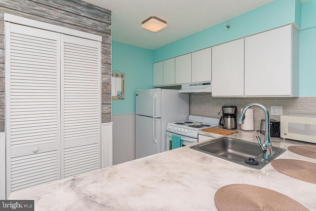 kitchen with white appliances, a sink, light countertops, under cabinet range hood, and wainscoting