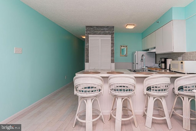 kitchen featuring light wood-type flooring, a kitchen bar, a sink, backsplash, and white appliances