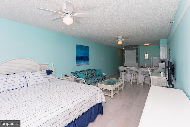 bedroom with light wood-style flooring, a textured ceiling, freestanding refrigerator, and a ceiling fan