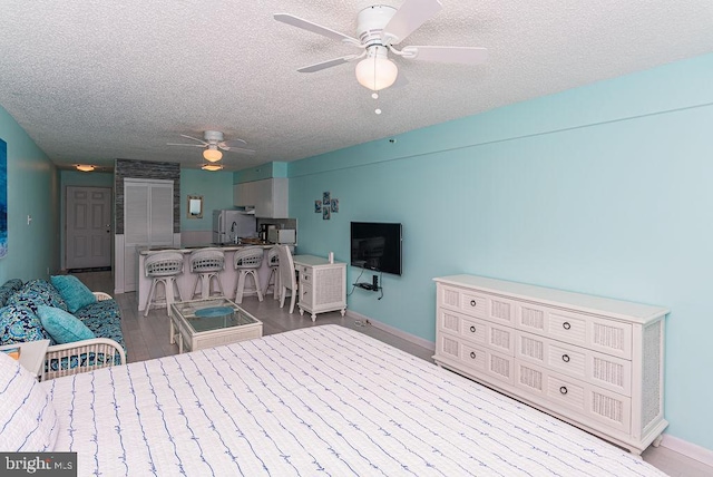 bedroom featuring baseboards, freestanding refrigerator, wood finished floors, a textured ceiling, and a sink