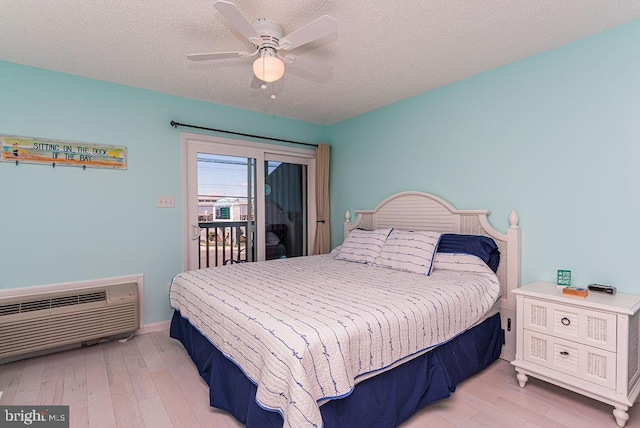 bedroom with a wall unit AC, a textured ceiling, wood finished floors, and access to outside