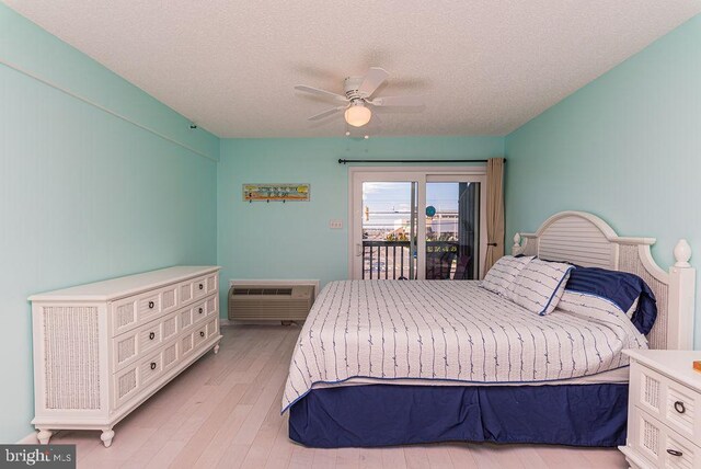 bedroom featuring ceiling fan, a wall unit AC, light wood-style floors, a textured ceiling, and access to outside