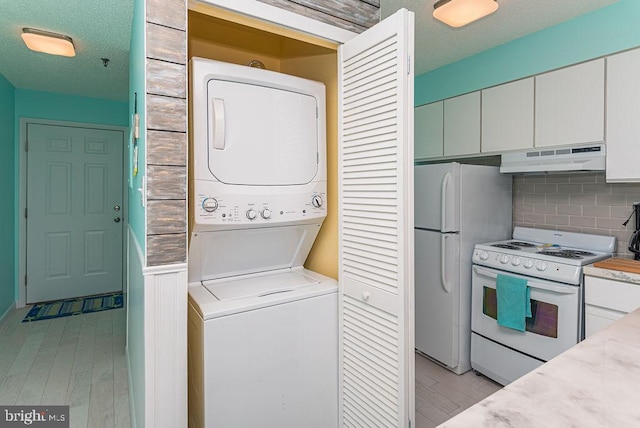 washroom with laundry area, light wood-style flooring, stacked washer / drying machine, and a textured ceiling