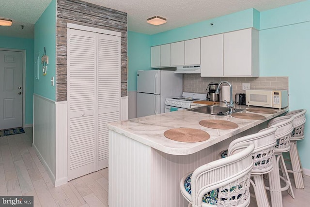 kitchen featuring white appliances, a sink, under cabinet range hood, a textured ceiling, and light wood-type flooring