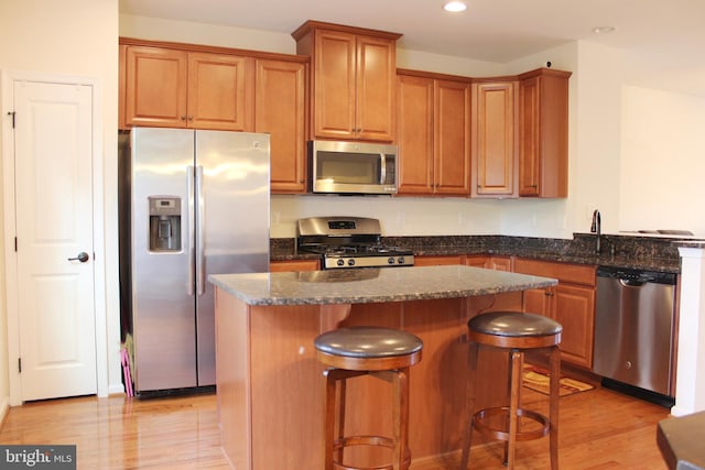 kitchen featuring light wood-style flooring, dark stone countertops, a kitchen island, recessed lighting, and appliances with stainless steel finishes