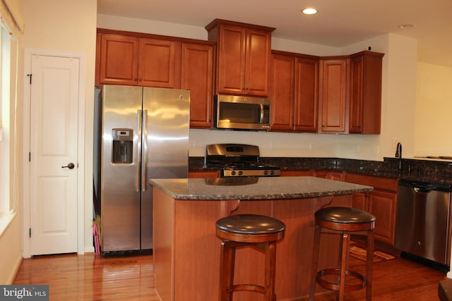 kitchen featuring wood finished floors, a kitchen island, dark stone counters, recessed lighting, and stainless steel appliances