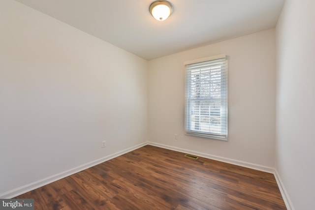 empty room with visible vents, dark wood-style floors, and baseboards