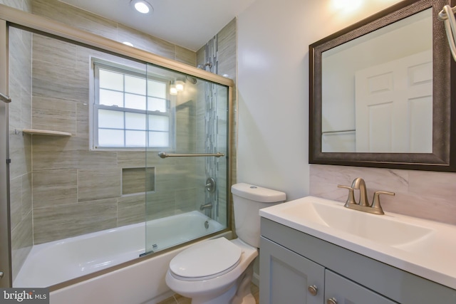 full bathroom with decorative backsplash, toilet, vanity, and bath / shower combo with glass door