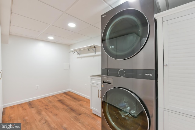 laundry area with baseboards, recessed lighting, cabinet space, stacked washer and dryer, and light wood-type flooring