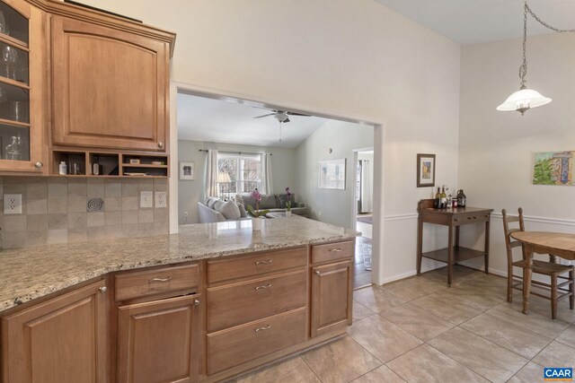 kitchen featuring backsplash, glass insert cabinets, ceiling fan, light stone counters, and a peninsula