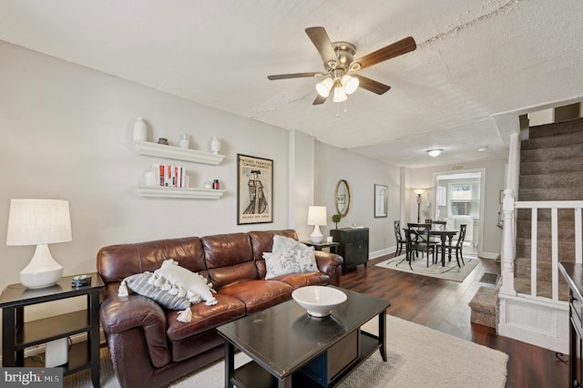 living room featuring stairway, a ceiling fan, baseboards, dark wood-type flooring, and a textured ceiling