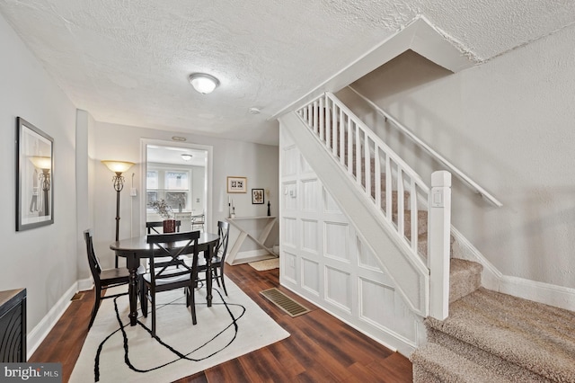 dining space with stairway, visible vents, baseboards, dark wood-style flooring, and a textured ceiling