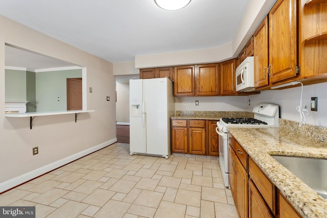 kitchen featuring light stone counters, baseboards, white appliances, and brown cabinets