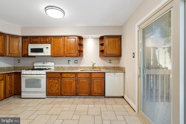 kitchen with white appliances, light stone countertops, brown cabinetry, open shelves, and a sink