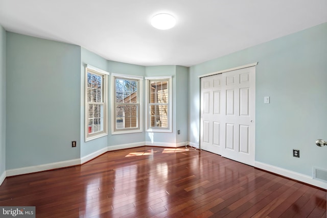 unfurnished bedroom featuring hardwood / wood-style floors, visible vents, baseboards, and a closet