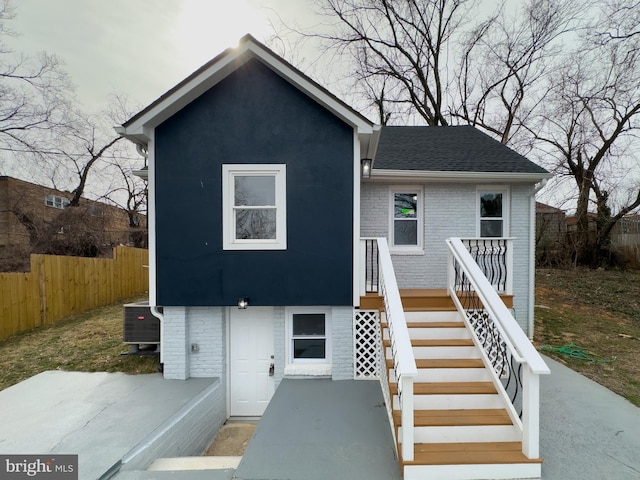 view of front facade featuring brick siding, fence, stairway, roof with shingles, and cooling unit