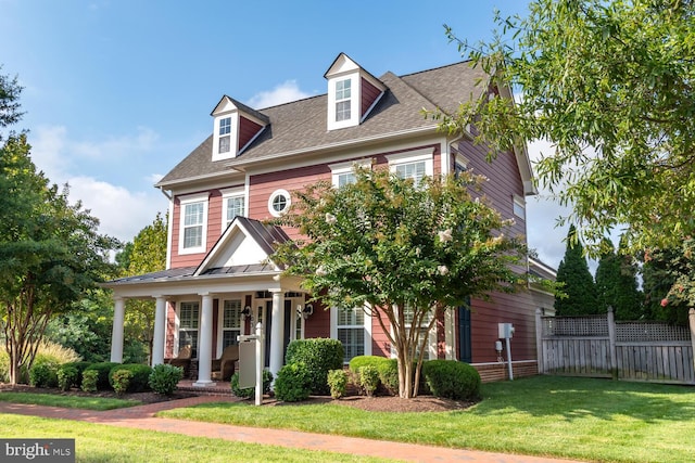 view of front of home with a front lawn, fence, covered porch, and a shingled roof