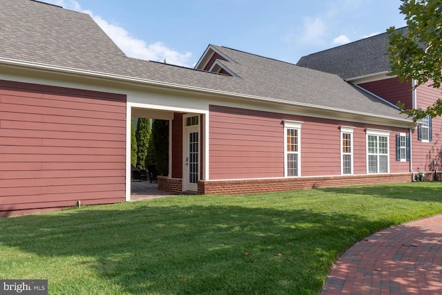 exterior space with a patio, brick siding, roof with shingles, and a lawn