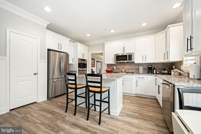 kitchen featuring white cabinetry, a kitchen breakfast bar, stainless steel appliances, and crown molding