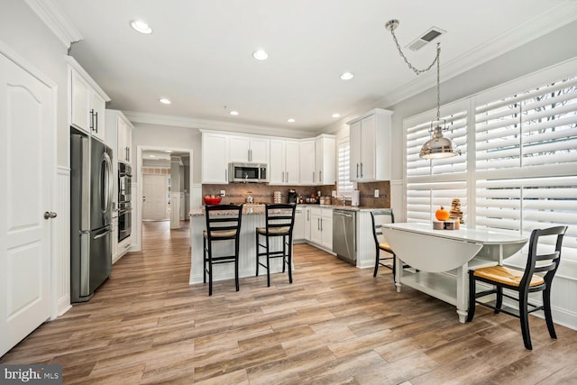 kitchen with light wood-type flooring, a kitchen bar, appliances with stainless steel finishes, white cabinets, and decorative backsplash