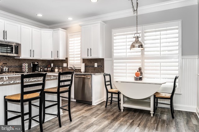 kitchen with crown molding, dark stone counters, stainless steel appliances, wood finished floors, and white cabinetry