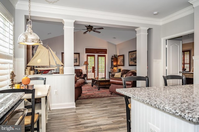 kitchen with wood finished floors, light stone countertops, decorative columns, ceiling fan, and crown molding