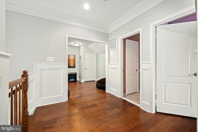 hallway featuring a decorative wall, wood finished floors, visible vents, and ornamental molding