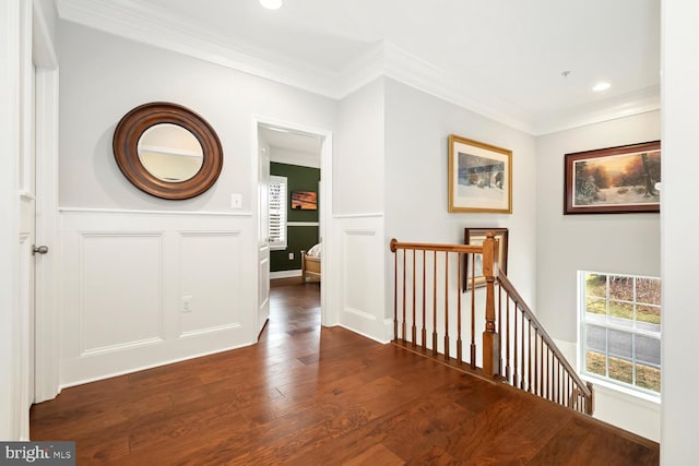 corridor with an upstairs landing, a decorative wall, crown molding, and dark wood-style flooring