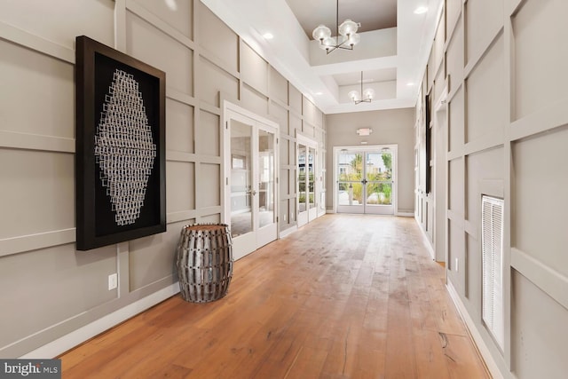 corridor featuring french doors, light wood-style floors, an inviting chandelier, and a decorative wall