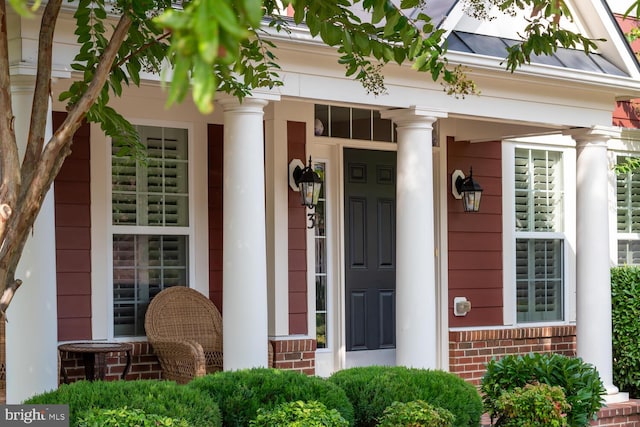 doorway to property featuring a standing seam roof, a porch, brick siding, and metal roof