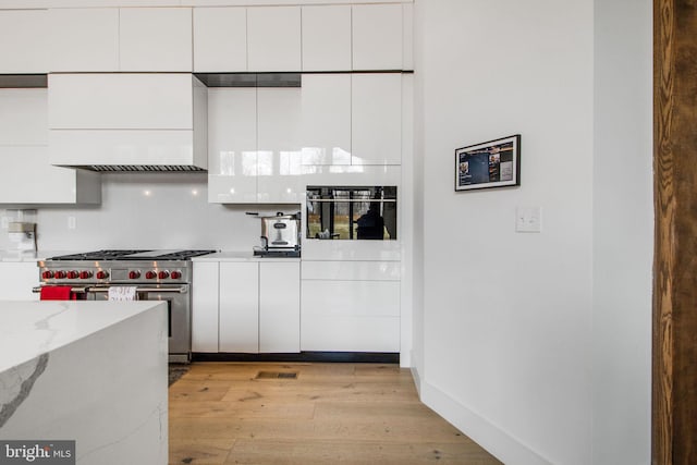 kitchen featuring light stone countertops, baseboards, light wood finished floors, stainless steel stove, and white cabinetry