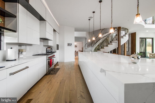 kitchen featuring light wood-type flooring, high end stove, modern cabinets, decorative light fixtures, and white cabinets