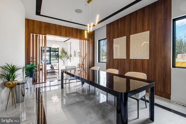 dining area featuring a wealth of natural light, visible vents, wood walls, and marble finish floor