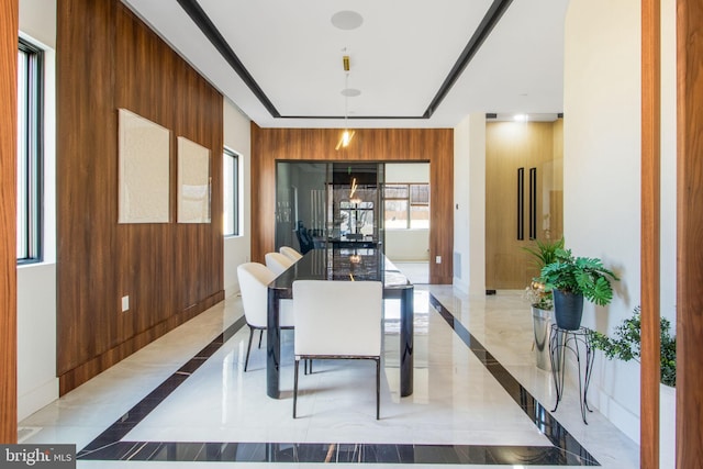 dining space with baseboards, elevator, wooden walls, and marble finish floor