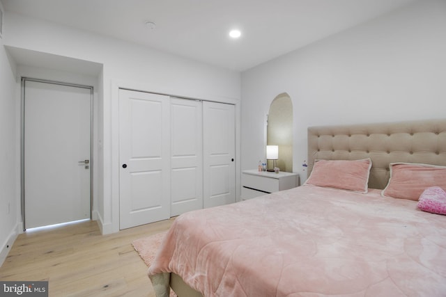 bedroom with recessed lighting, light wood-type flooring, arched walkways, and a closet