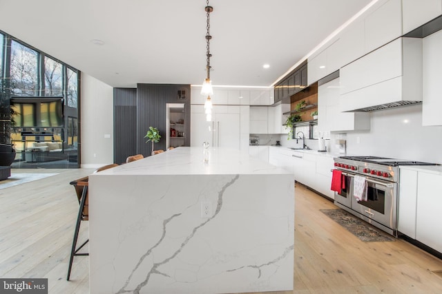 kitchen with a breakfast bar area, light wood-style flooring, a sink, luxury range, and modern cabinets