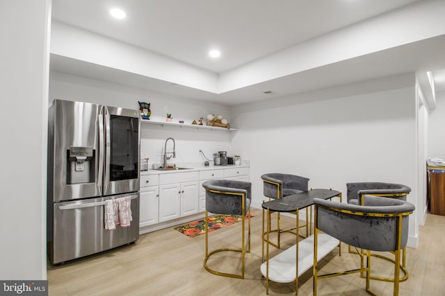 kitchen featuring light countertops, light wood-style floors, stainless steel refrigerator with ice dispenser, white cabinets, and a sink