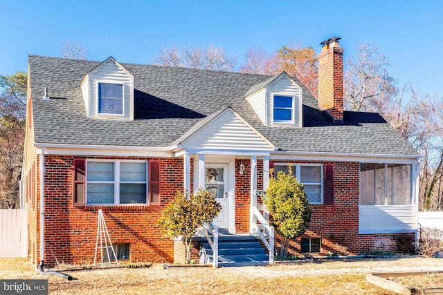 cape cod home featuring fence, brick siding, roof with shingles, and a chimney