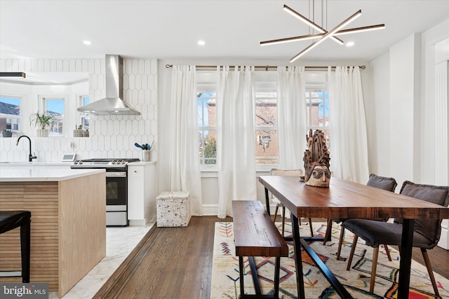 kitchen featuring backsplash, light wood-style floors, stainless steel stove, wall chimney exhaust hood, and light countertops