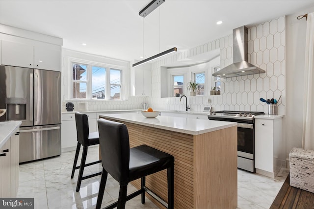 kitchen featuring marble finish floor, a breakfast bar, a kitchen island, appliances with stainless steel finishes, and wall chimney exhaust hood