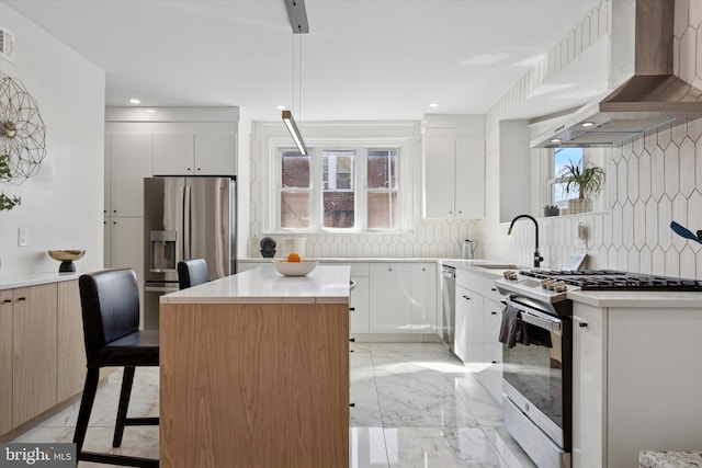 kitchen with a kitchen island, a sink, stainless steel appliances, wall chimney exhaust hood, and marble finish floor