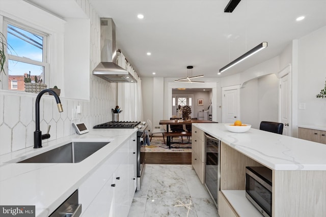 kitchen featuring modern cabinets, wall chimney exhaust hood, stainless steel appliances, and a sink